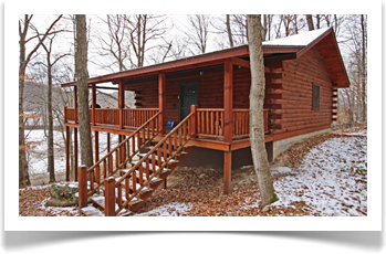 tall trees surronding two story lodge with 4 windows, wrap around deck
