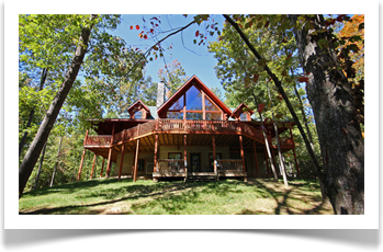 tall trees surronding two story lodge with 4 windows, wrap around deck