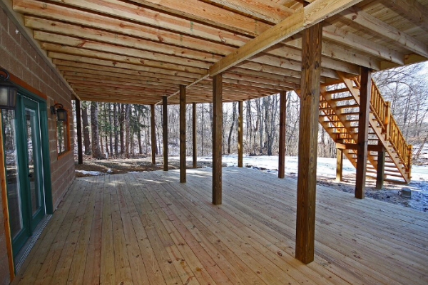 Closeup of Lower Level Porch, facing West. Walkout Door and Picture Windows from Lower Level on left, with Fire Pit area stairs coming down on right. South woods ahead