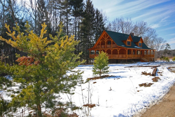 Northeast View of Lodge exterior, from Driveway. Pine Trees in foreground. Lodge with 2 Gables on front, Wrap-Around Main Deck, Loft Level Deck on this end. Log-Frame Construction