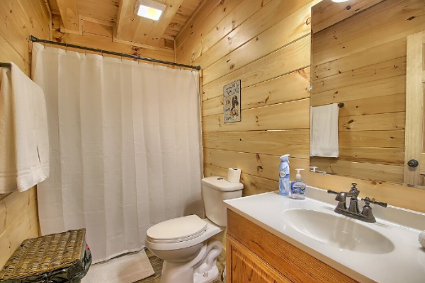 Bathroom 2, on Main Floor, with Tub and Shower, Toilet, Sink and Large Mirror, Tile Floor. Wicker Clothes Hamper