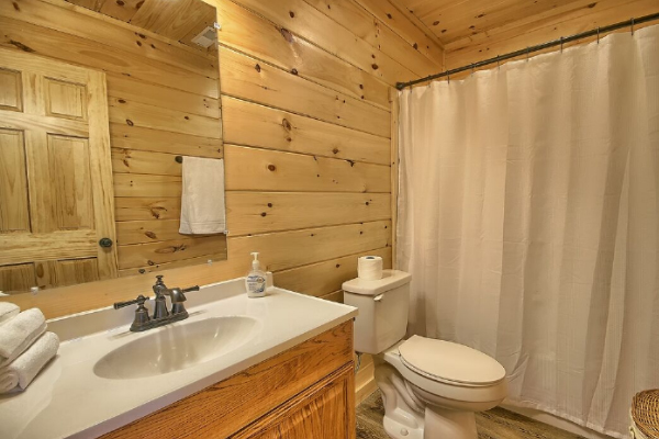 Bathroom 1, on Lower Level, with Tub and Shower, Toilet, Sink and Large Mirror, Tile Floor. Wicker Clothes Hamper