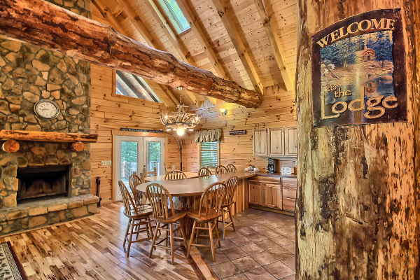 Main Floor Entrance, with Welcome Sign on Log Post, and Great Room Fireplace and Dining Room beyond, as well as South Side Exit Doors. Big Log Beam is above, going from Front to Rear of Lodge